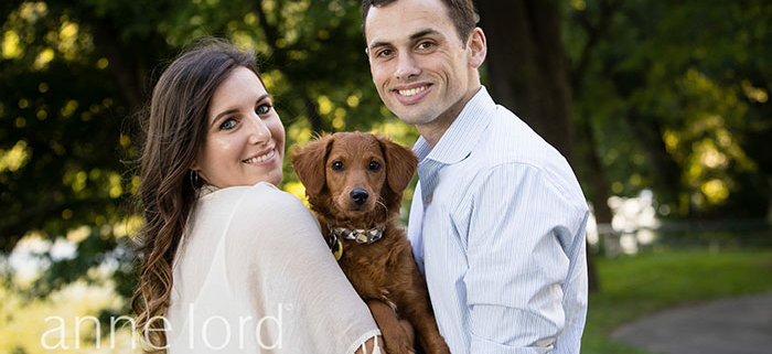 A newly engaged couple holding a cute dog. Photograph by Anne Lord Photography